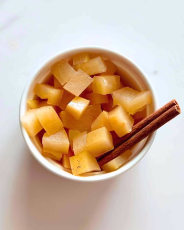 Homemade stewed apples in a white ramekin with a cinnamon stick as garnish.